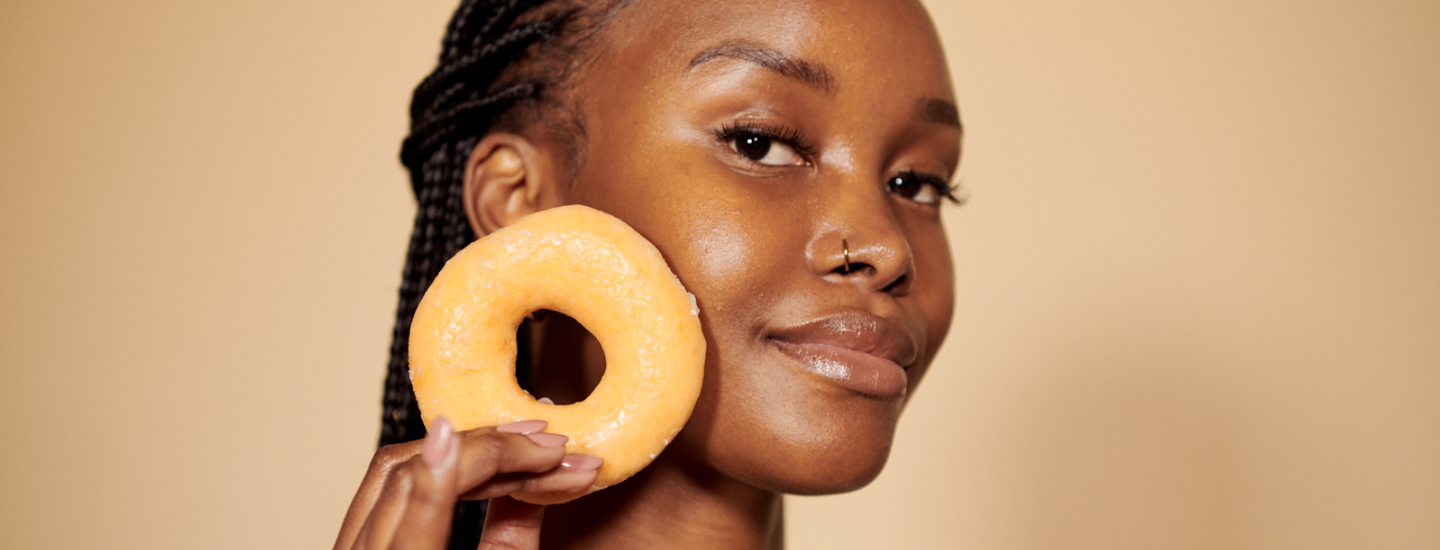 woman with braids holding a glazed ring donut, glazed donut skin, donut skin, glazed donut, skin, skin trends, beauty trend, the suite, the suite edit, brutal fruit